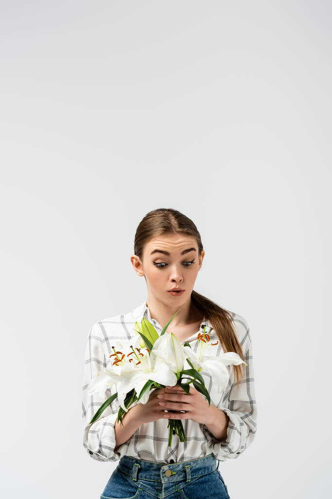 Schockiertes attraktives Mädchen posiert wie eine Marionette mit Blumen isoliert auf grau - Foto, Bild