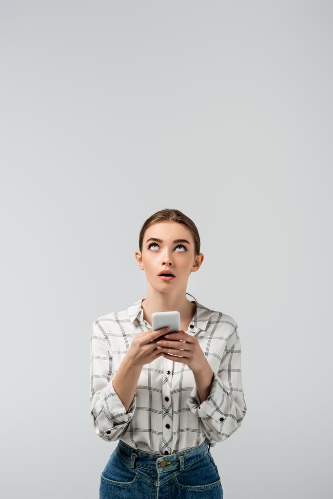 yllättynyt houkutteleva tyttö käyttää älypuhelinta ja etsii ylös eristetty harmaa - Valokuva, kuva
