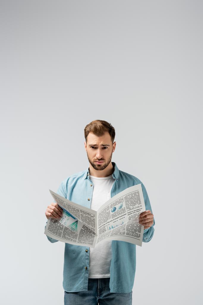 σύγχυση νεαρός άνδρας ανάγνωση εφημερίδα απομονώνονται σε γκρι - Φωτογραφία, εικόνα