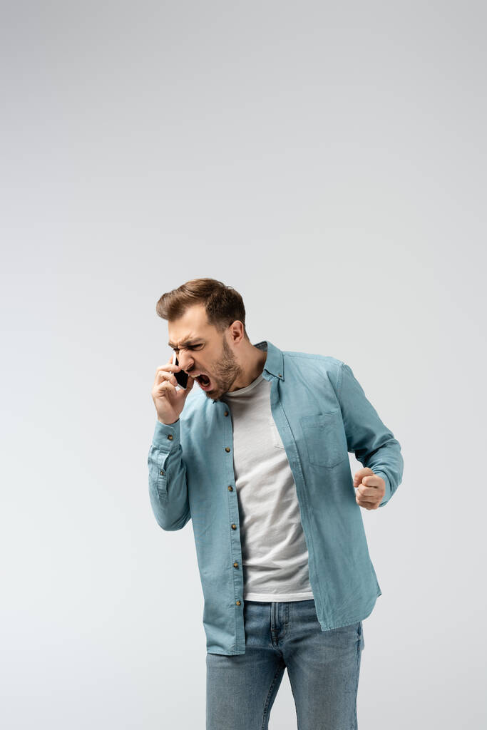 angry young man screaming on smartphone isolated on grey - Photo, Image