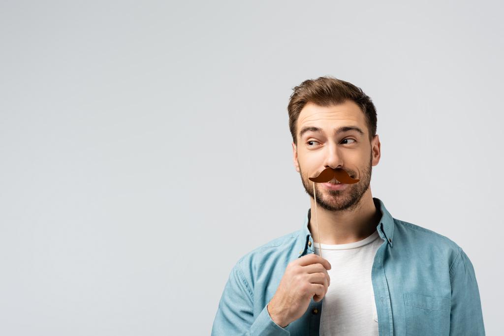 смішний молодий чоловік з підробленими вусами на паличці дивиться ізольовано на сірий
 - Фото, зображення
