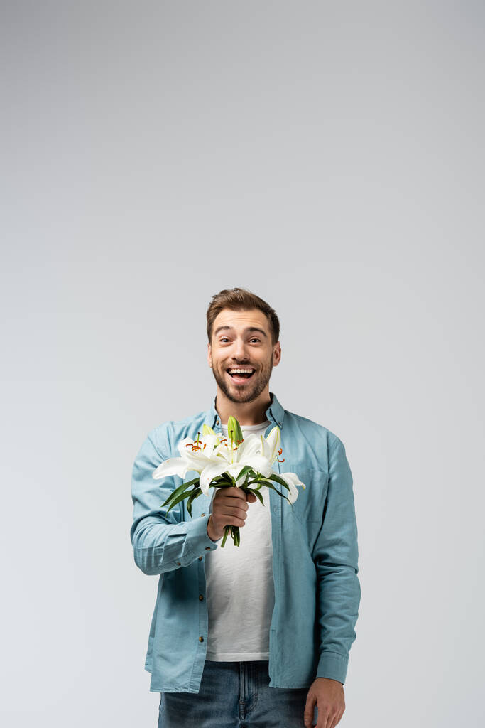 щасливий молодий чоловік з квітковим букетом ізольований на сірому
 - Фото, зображення
