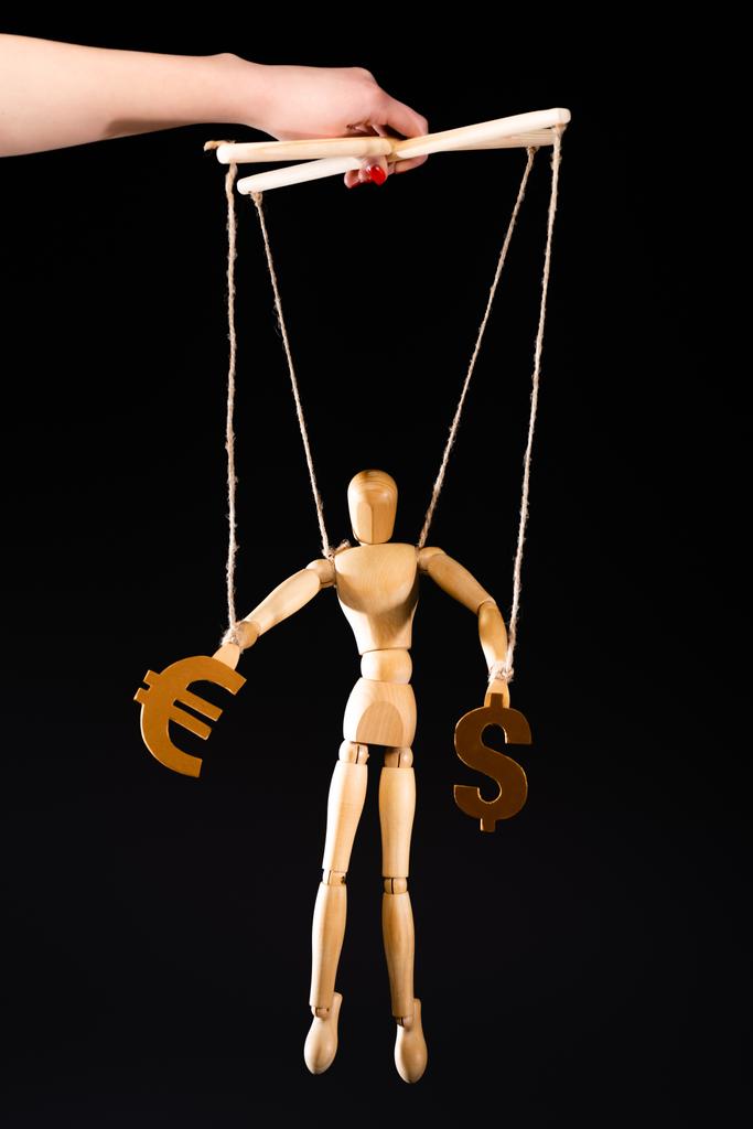 cropped view of puppeteer holding wooden marionette on strings with currency signs isolated on black - Photo, Image