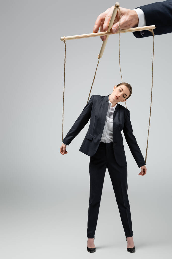 vista ritagliata di burattinaio azienda donna d'affari marionetta su corde isolate su grigio - Foto, immagini