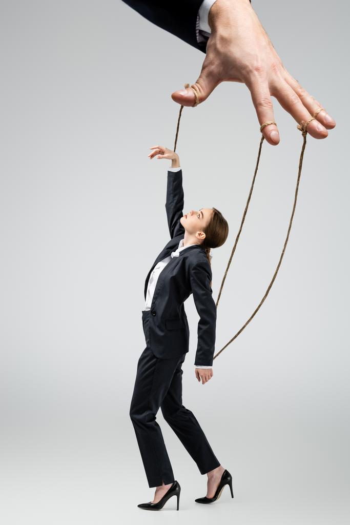 cropped view of puppeteer holding businesswoman marionette on strings isolated on grey - Photo, Image