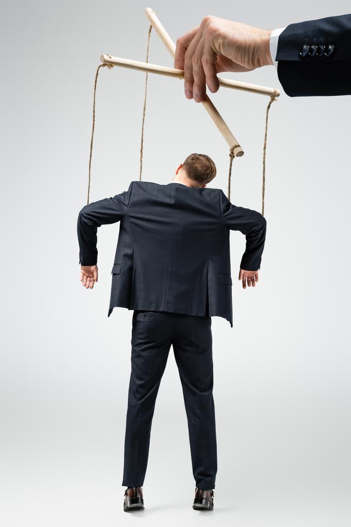 vista recortada del titiritero sosteniendo marioneta de hombre de negocios en cuerdas aisladas en gris
 - Foto, imagen