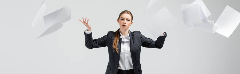 displeased businesswoman in suit throwing papers in air isolated on grey, panoramic shot - Photo, Image