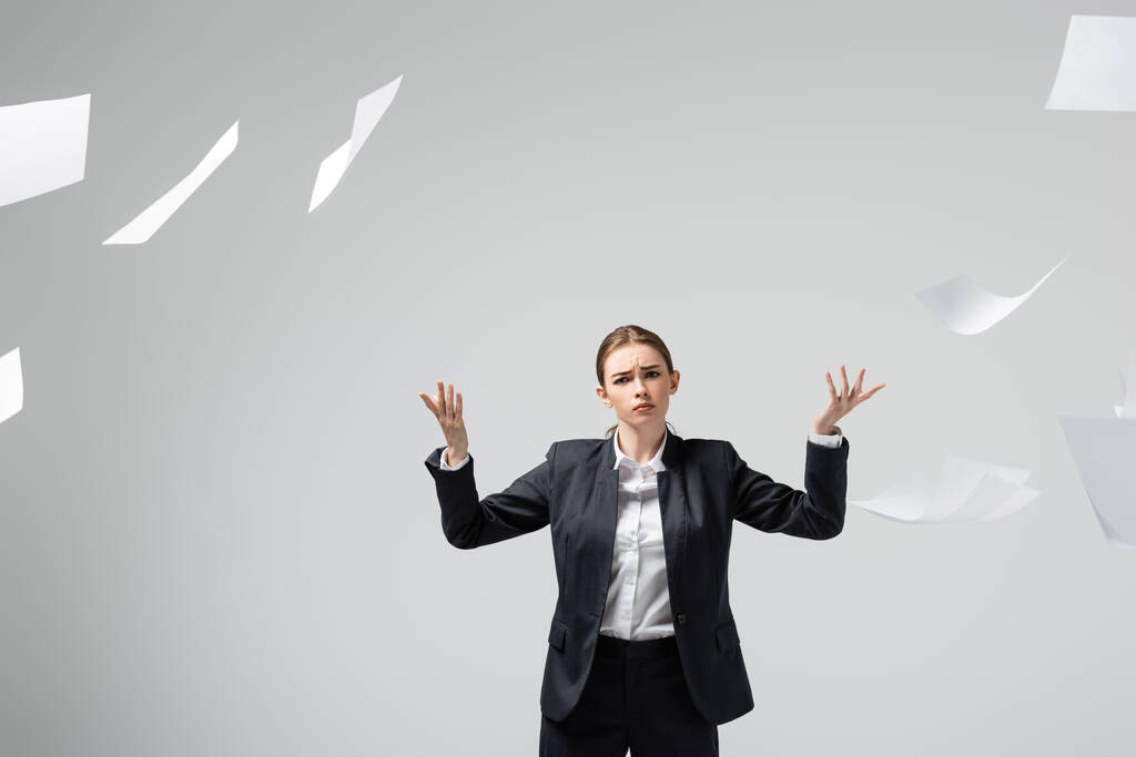 mujer de negocios disgustada en traje arrojando papeles en el aire aislado en gris
 - Foto, Imagen