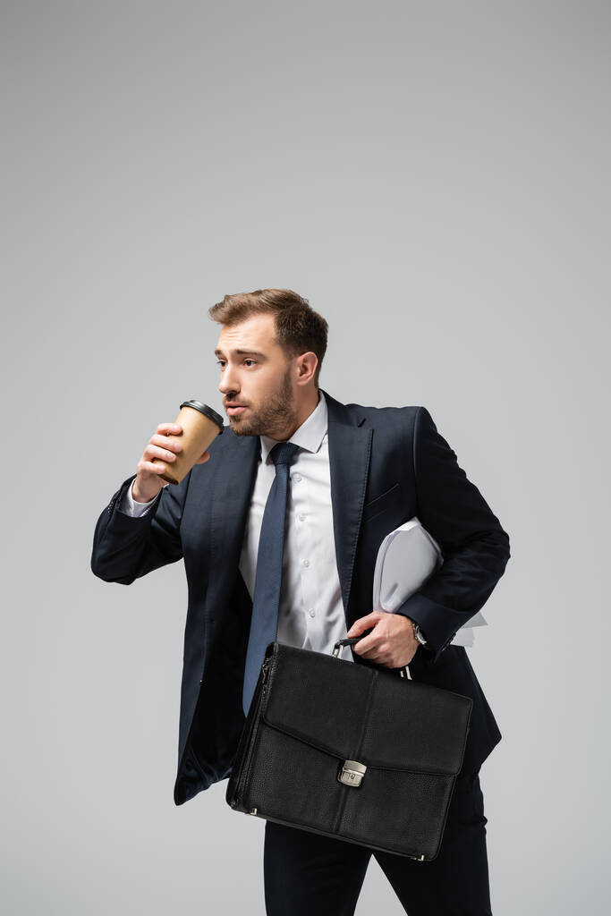 επιχειρηματίας με δερμάτινη βαλίτσα και χάρτινο κύπελλο απομονωμένο σε γκρι - Φωτογραφία, εικόνα