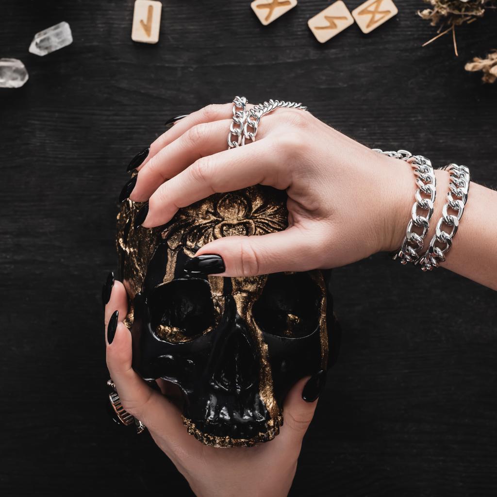 close up of woman holding skull near runes and crystals on black  - Photo, Image