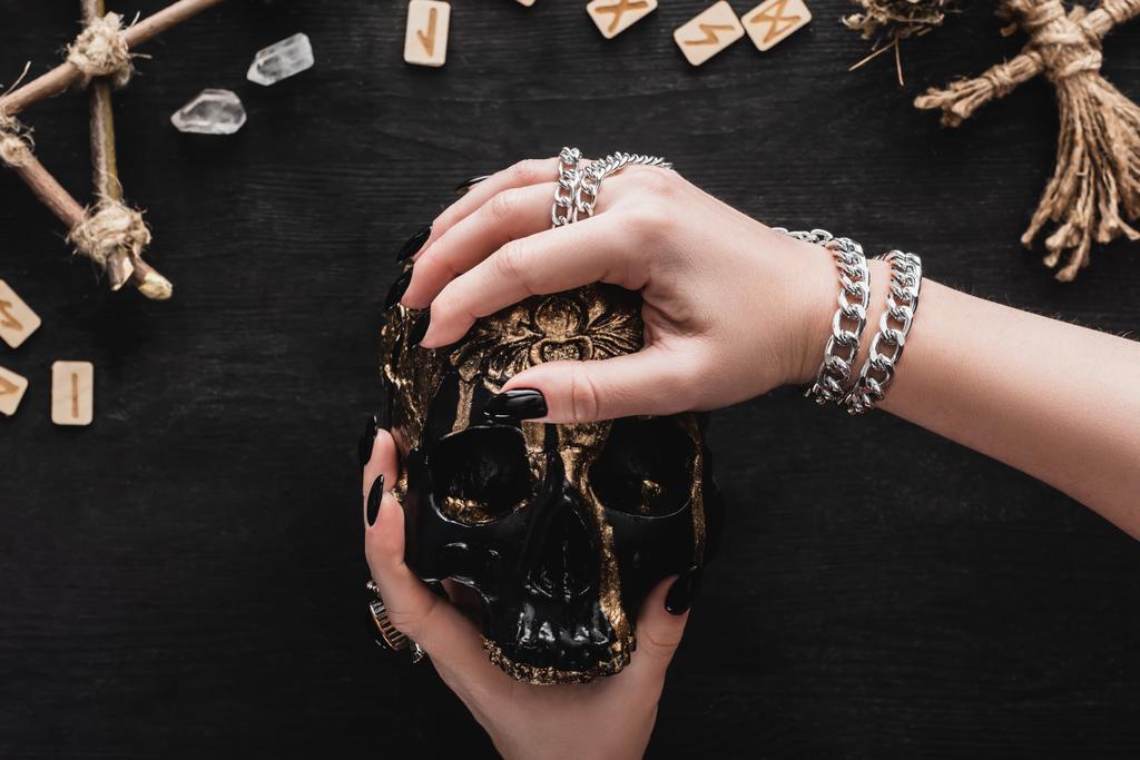 Ausgeschnittene Ansicht einer Frau mit Totenkopf in der Nähe von Kristallen und Runen auf Schwarz  - Foto, Bild