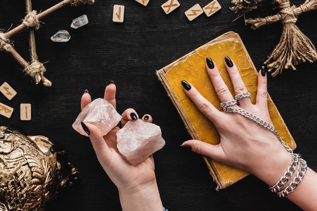 górny widok czarownic trzymających kryształy i dotykających starą księgę czarnej magii w pobliżu lalki voodoo i runy na czarny  - Zdjęcie, obraz