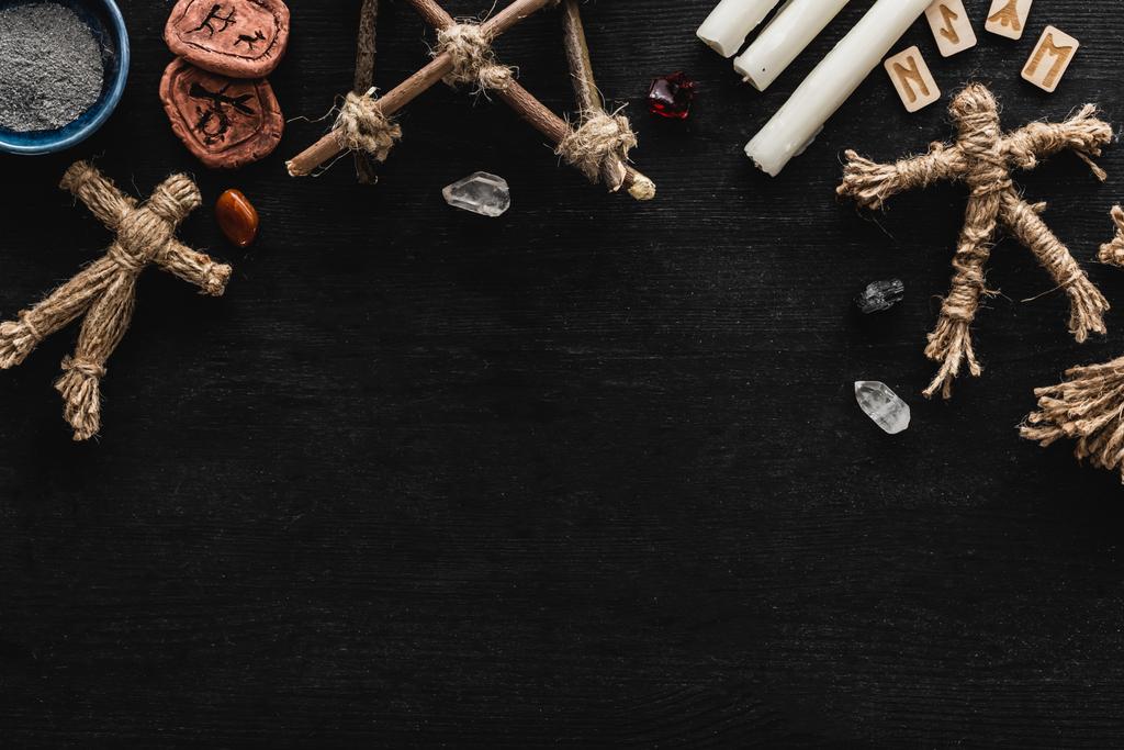 vue de dessus des poupées vaudou près du bol avec des cendres, des cristaux, des bougies et de vieilles runes sur noir  - Photo, image