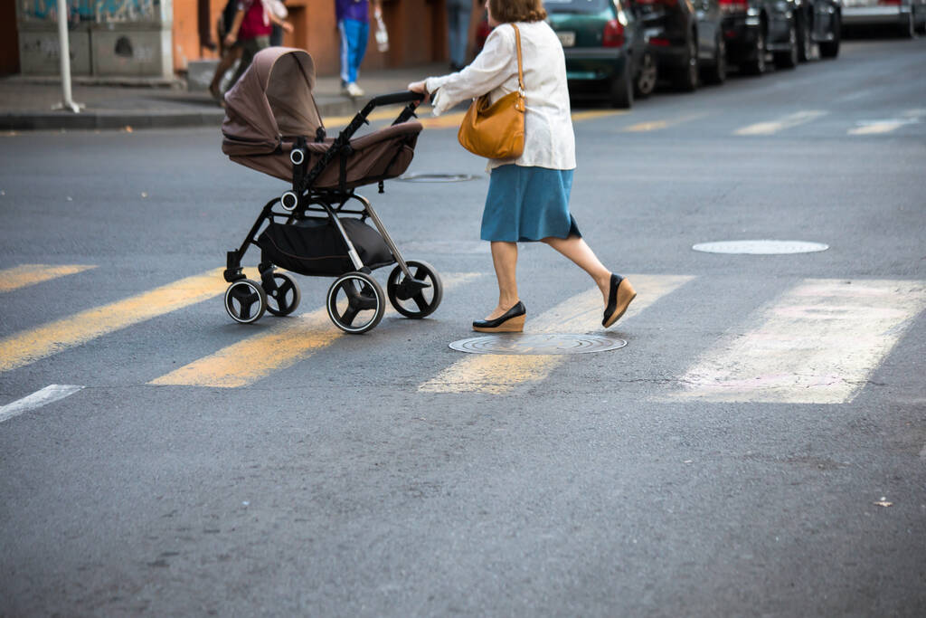 Woman with baby carriage crossing the street at a crosswalk.  - Photo, Image
