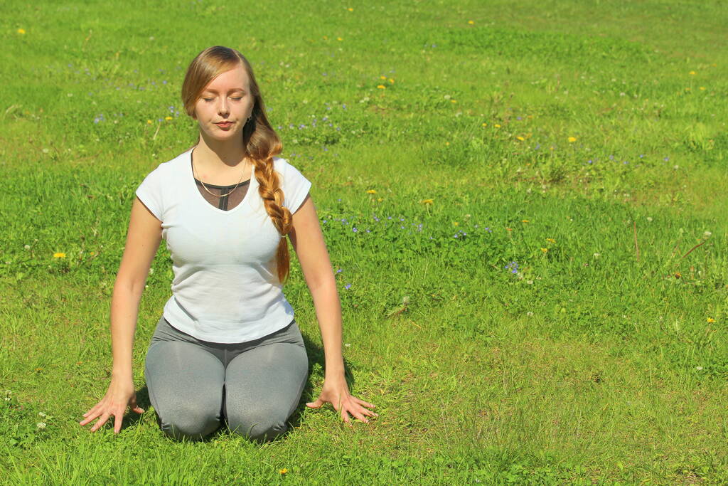 Mladá žena evropského vzhledu dělá jógu v letní přírodě. Žena sedící v hrdinské póze, Virasana. Vysoce kvalitní fotografie pro web a tisk s prázdným prostorem pro text a design. - Fotografie, Obrázek