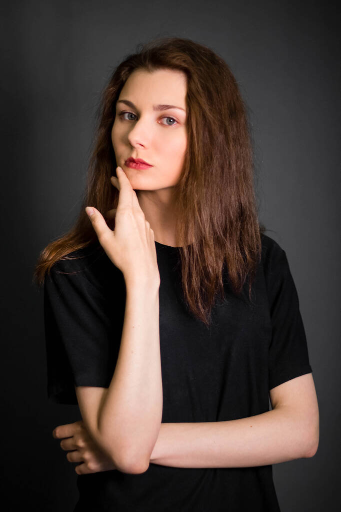 Portrait of a beautiful, young woman in black clothes with long hair. Studio photo, on a gray background. A model with clean skin. - Photo, Image