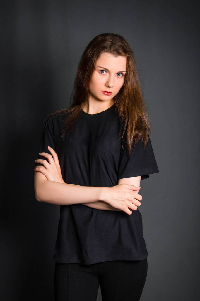 Mooie, jonge vrouw met lang haar, in zwarte kleren, poserend in studio op een grijze achtergrond. Een model met een schone huid. - Foto, afbeelding