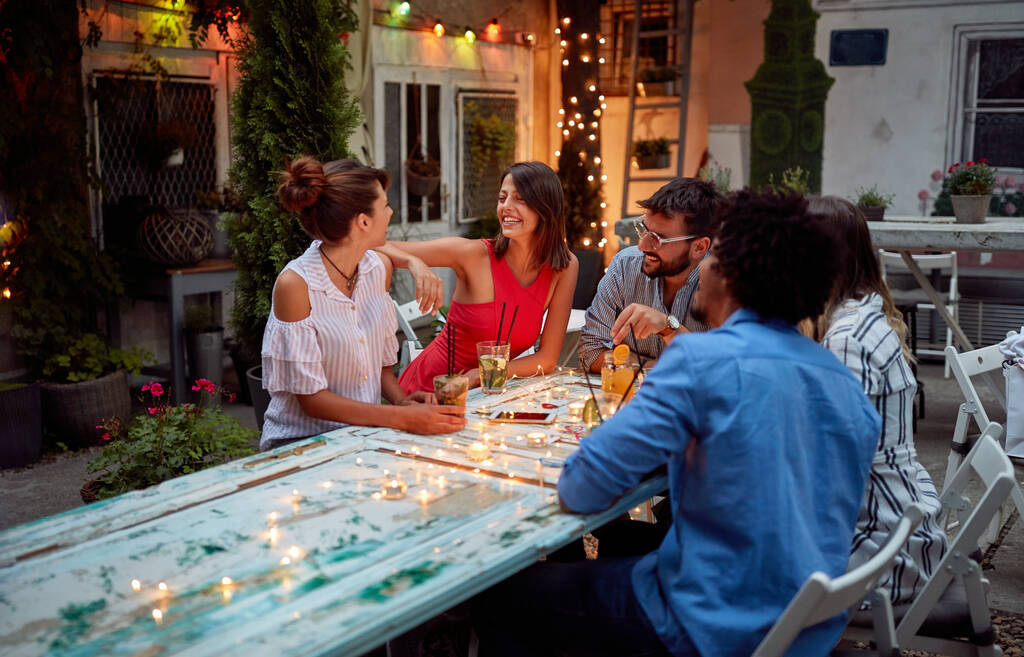 Οι νεαροί φίλοι απολαμβάνουν τη φιλική συνομιλία το σούρουπο στον κήπο του καφέ - Φωτογραφία, εικόνα