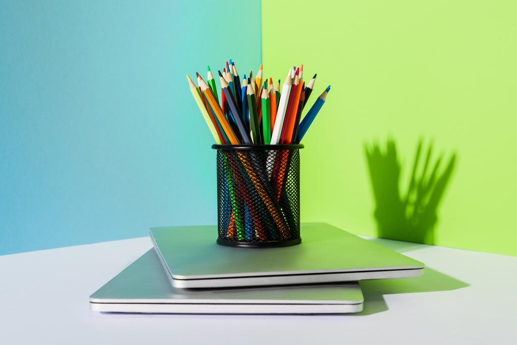 держатель карандаша с цветными карандашами на современных ноутбуках на синем, зеленом и белом фоне
 - Фото, изображение