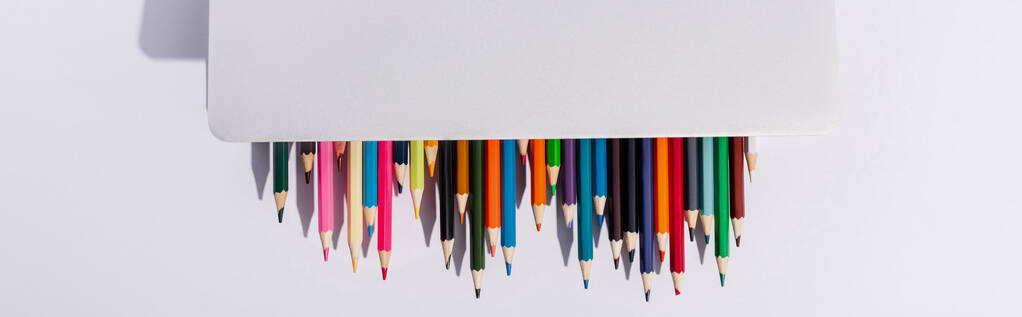вид зверху кольорових олівців в сучасному ноутбуці на білому тлі, панорамний знімок
 - Фото, зображення