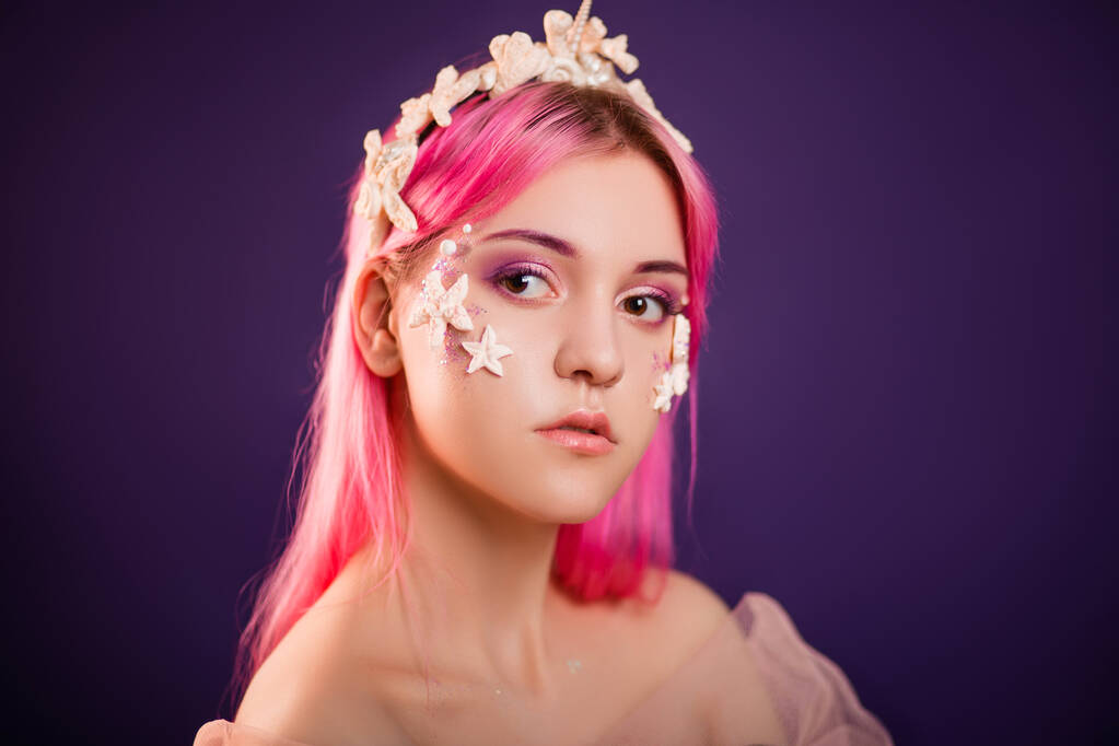 Nahaufnahme Porträt eines jungen schönen Mädchens mit rosa Haaren und professionellem Make-up, Meerprinzessin mit Seesternen und Muscheln auf Gesicht und Kopf. Halloween-Make-up. - Foto, Bild