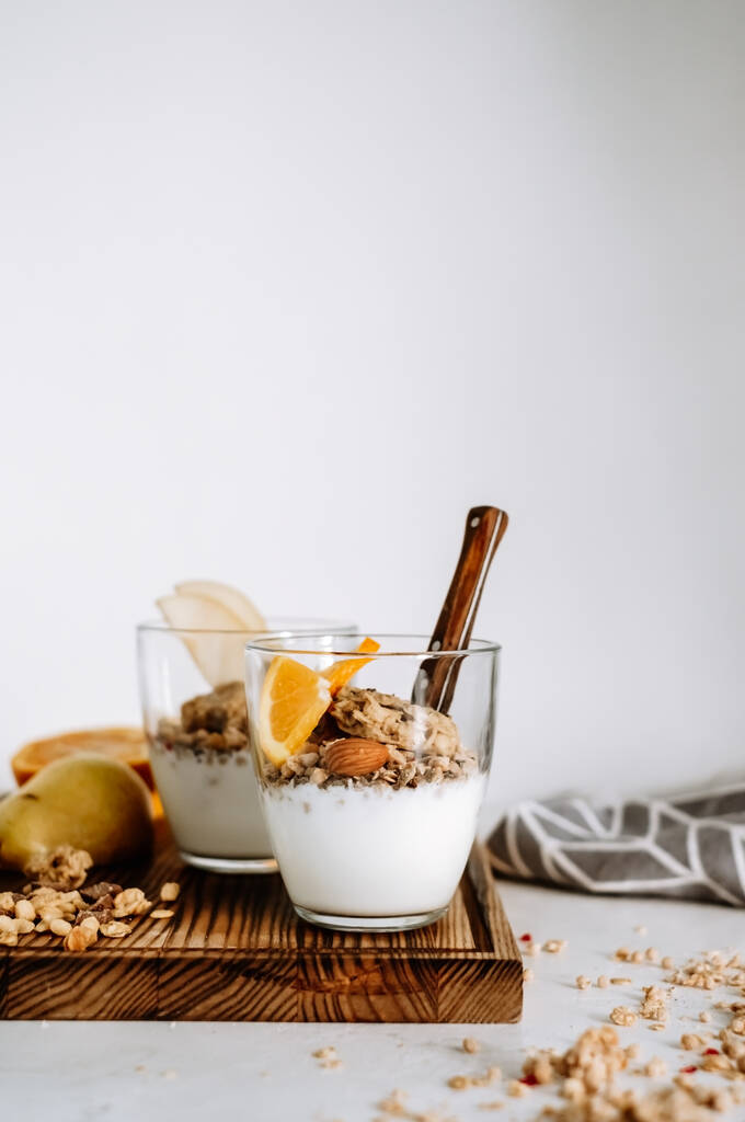 Muesli i naturalny jogurt z plasterkami owoców i orzechów w szklanym kubku na drewnianej desce, zdrowe śniadanie. Wysokiej jakości zdjęcie - Zdjęcie, obraz
