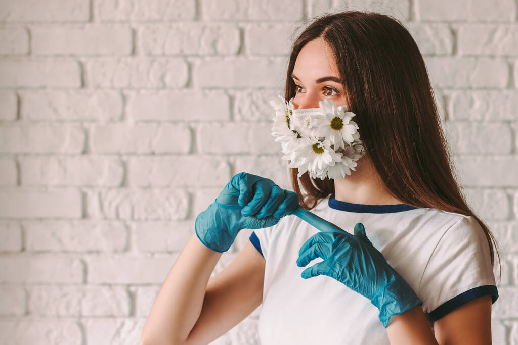 Portret szczęśliwej kobiety lekarz w masce medycznej twarzy z kwiatami zdejmujące lateksowe rękawice ochronne. Piękna dziewczyna w letniej masce ochronnej zdejmując rękawiczki medyczne. Wygrać, zakończyć walkę koronawirusów COVID-19 - Zdjęcie, obraz
