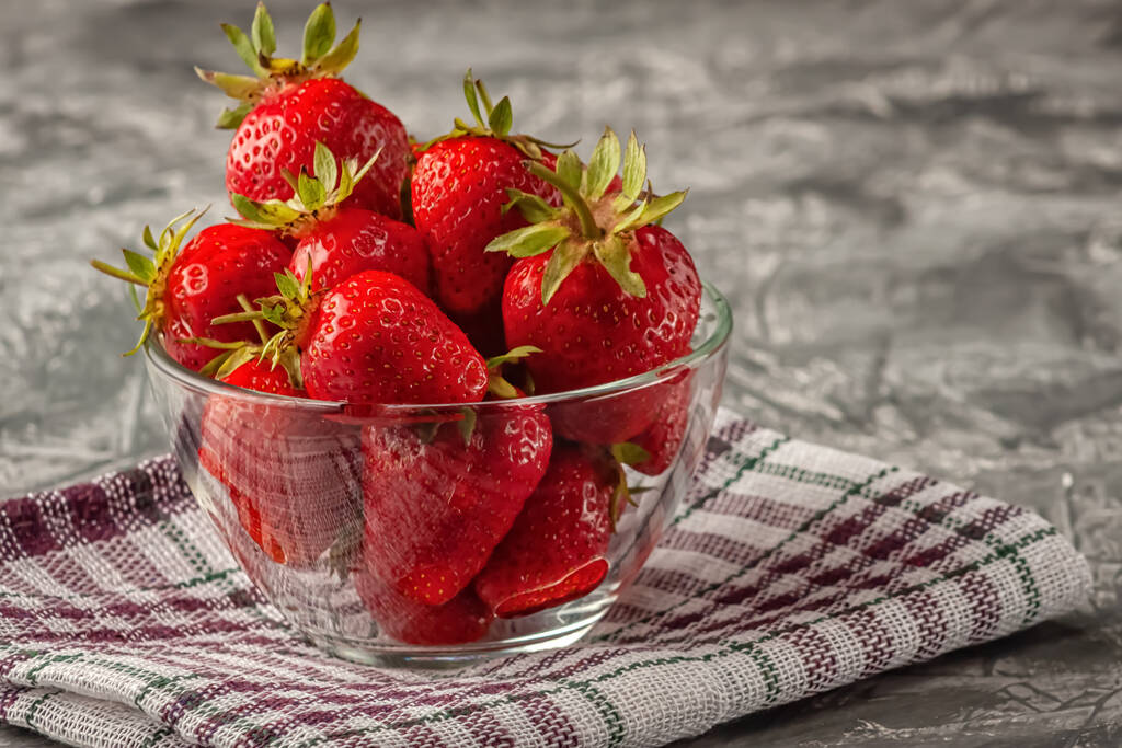Σε γκρι φόντο, φρέσκες ώριμες και νόστιμες φράουλες σε γυάλινο μπολ - Φωτογραφία, εικόνα