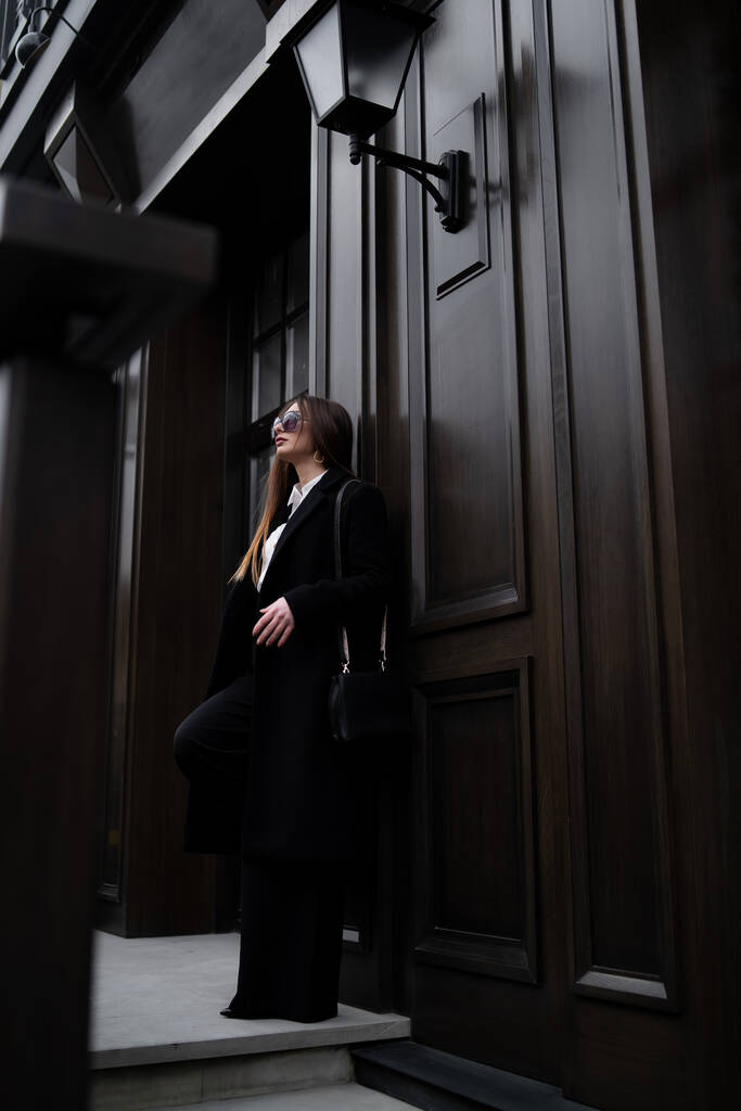 Foto esterna di signora bruna che cammina sullo sfondo della strada in fredda giornata autunnale. Ritratto di moda street style. indossando pantaloni casual scuri, - Foto, immagini