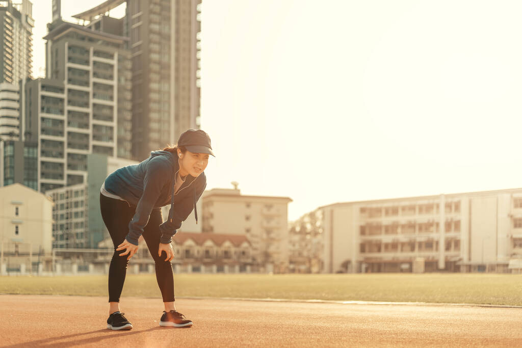 Μια γυναίκα κάνει ένα διάλειμμα από το τρέξιμο σε εξωτερικούς χώρους και προπόνηση σε αγώνα στίβου στο στάδιο και το ηλιοβασίλεμα. - Φωτογραφία, εικόνα