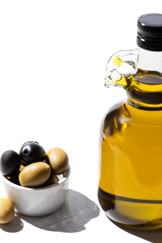 huile d'olive en bouteille près des olives vertes et noires dans un bol sur fond blanc - Photo, image