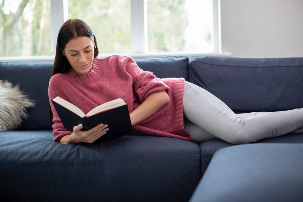 Donna rilassante sdraiata sul divano a casa libro di lettura - Foto, immagini
