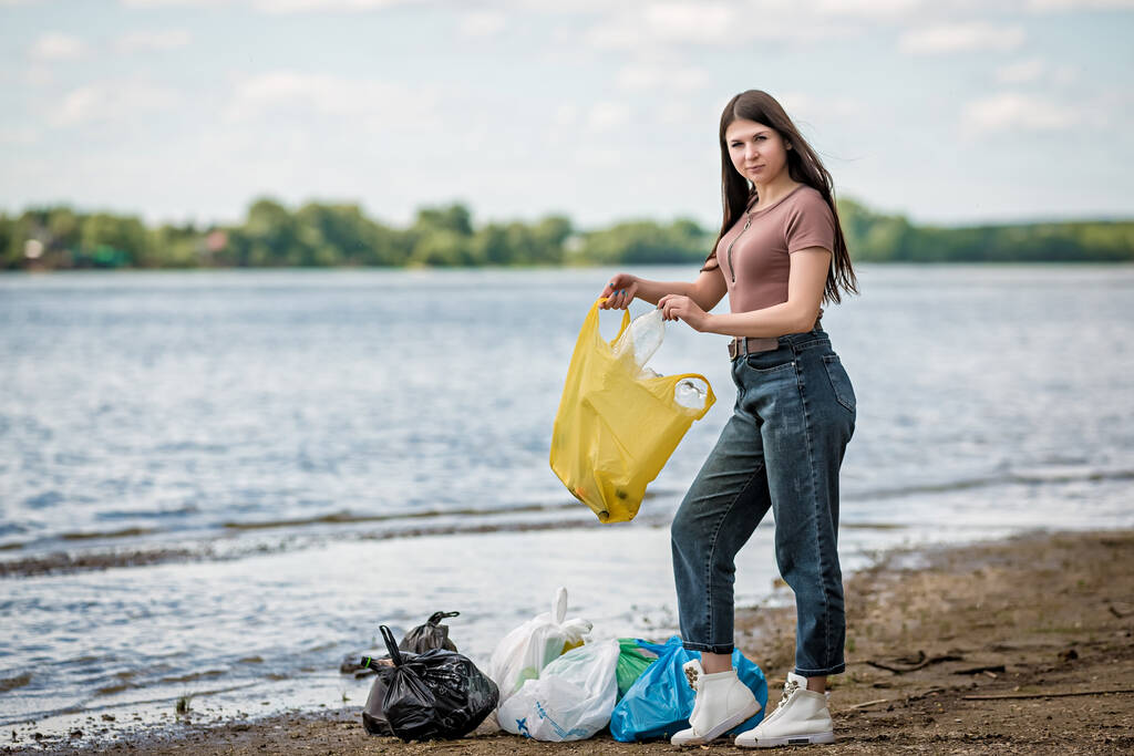 Девушка собирает мусор на пляже. Девушка очищает пляж от мусора
 - Фото, изображение