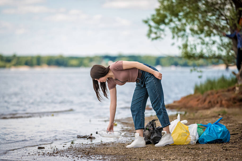 少女は浜辺でゴミを集めてる。少女はゴミの海をきれいにし - 写真・画像