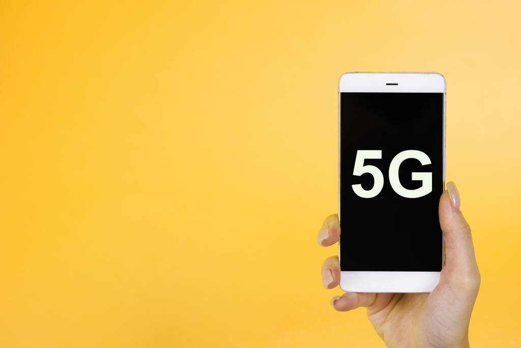 Fundo criativo, mão segurando um telefone com um símbolo 5G. O conceito de rede 5G, Internet móvel de alta velocidade, redes de nova geração
 - Foto, Imagem