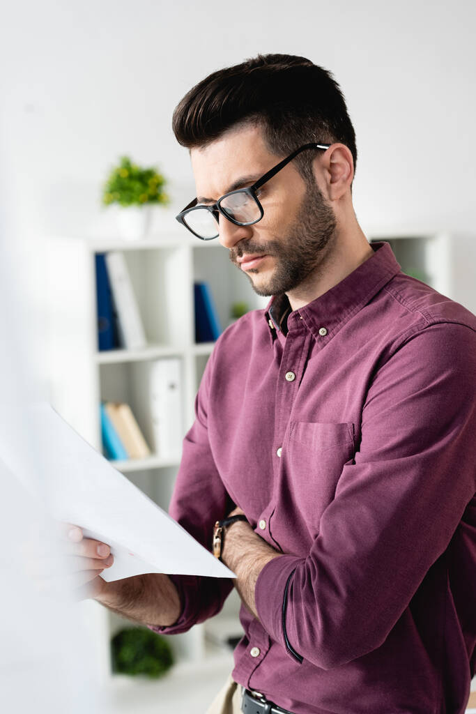 избирательный фокус концентрированного бизнесмена в очках, смотрящего на документ в офисе
 - Фото, изображение