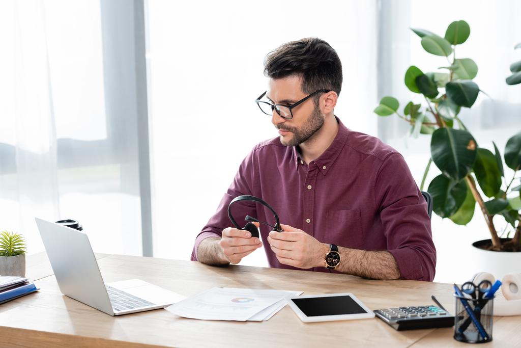 młody, poważny biznesmen trzymający słuchawki podczas oglądania laptopa podczas rozmowy wideo - Zdjęcie, obraz