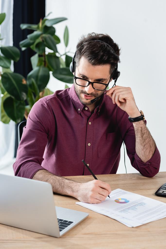 attente zakenman in headset schrijven op papier tijdens online vergadering op laptop - Foto, afbeelding