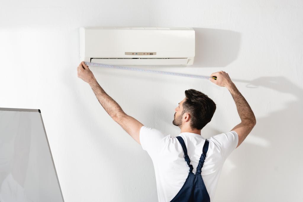 jovem reparador de medição de ar condicionado fixado na parede branca no escritório
 - Foto, Imagem