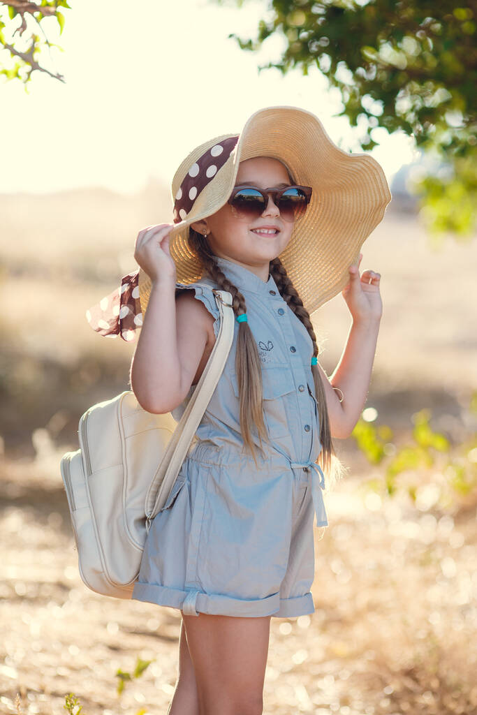 Красива маленька дівчинка в смугастій сукні і капелюсі, що розслабляється на пляжі біля моря, влітку, мила маленька дівчинка на пляжі
 - Фото, зображення