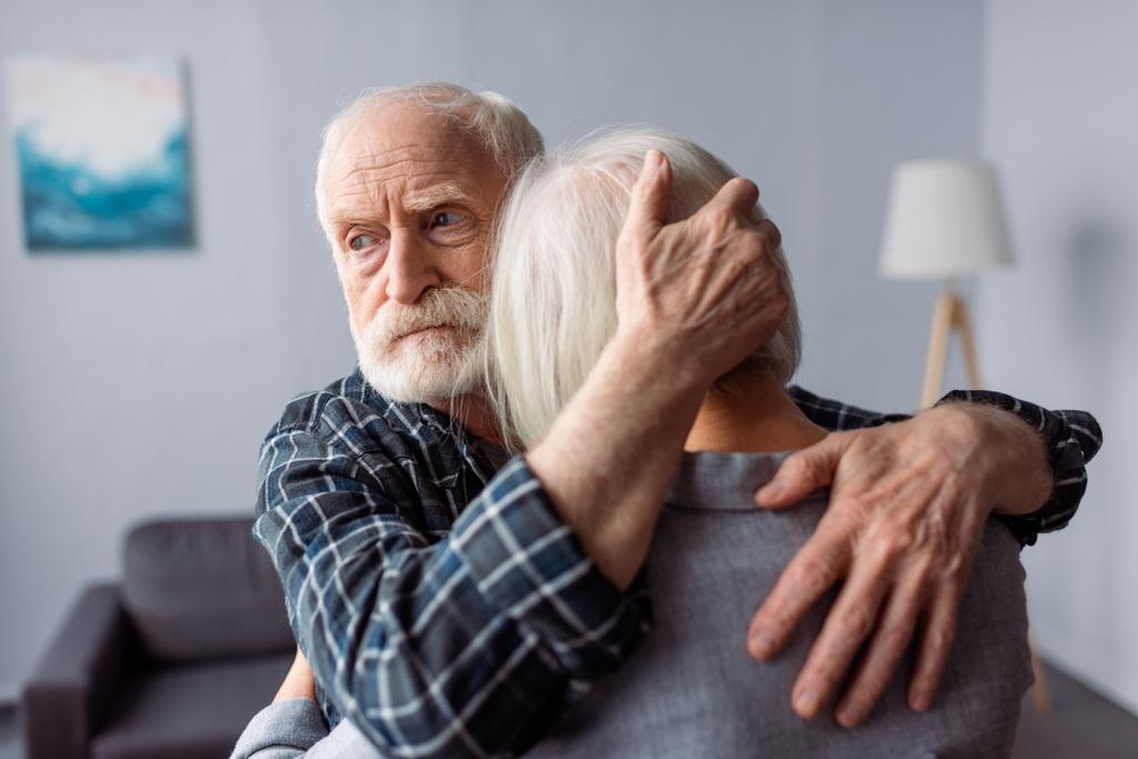 старший, грустный мужчина обнимает жену, болеет слабоумием, и смотрит в сторону
 - Фото, изображение
