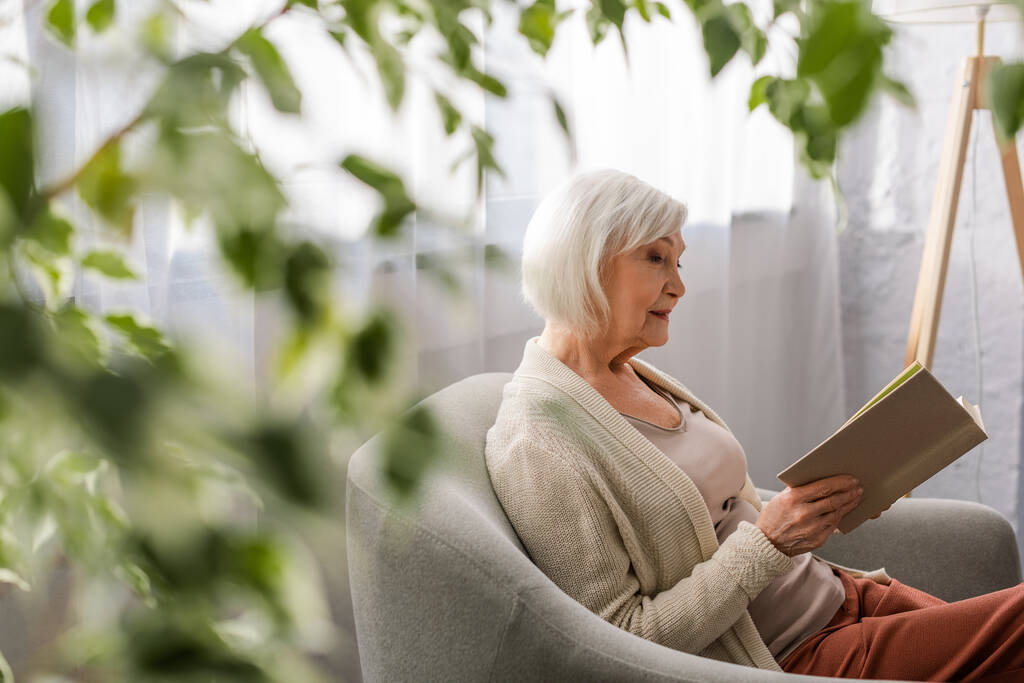 enfoque selectivo de la mujer mayor atenta sentada en sillón y libro de lectura
 - Foto, Imagen