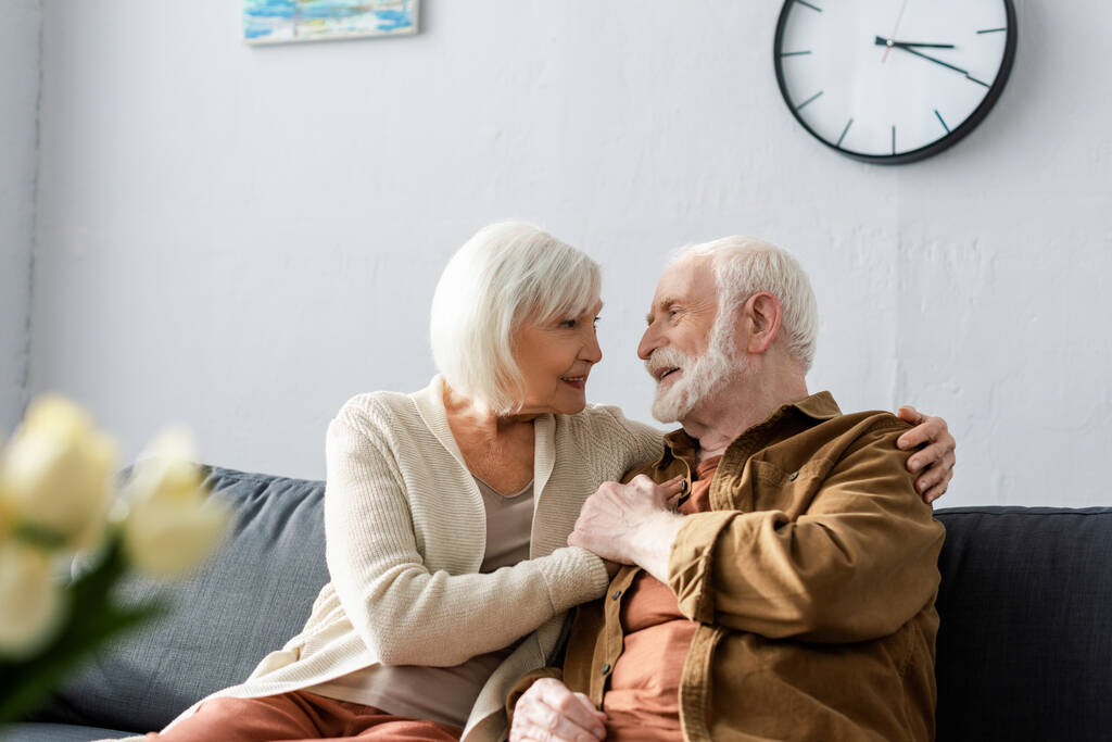 избирательный фокус счастливой пожилой пары, сидящей на диване и смотрящей друг на друга
 - Фото, изображение