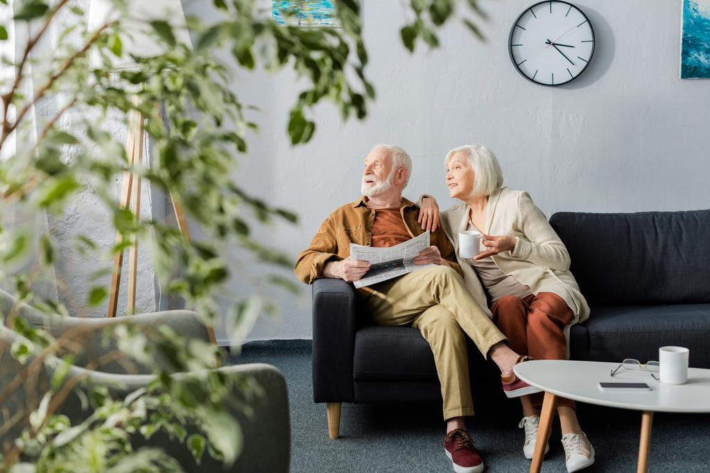 επιλεκτική εστίαση του ηλικιωμένου ζευγαριού κοιτάζοντας μακριά, ενώ κάθεται στον καναπέ - Φωτογραφία, εικόνα