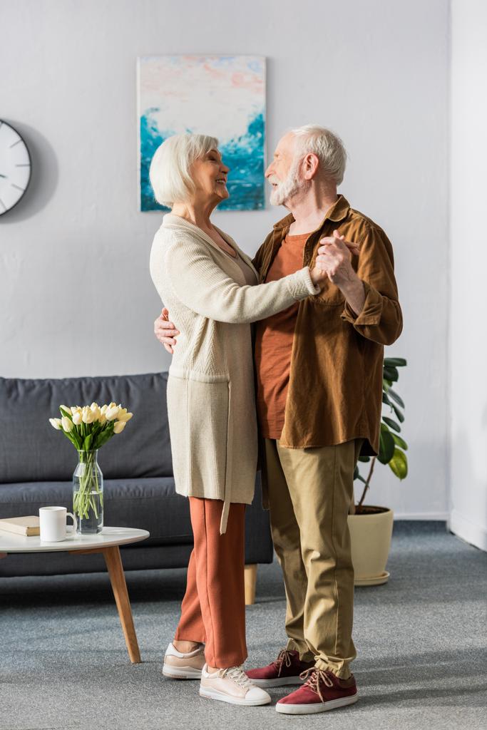 felice coppia anziana che balla mentre si guarda vicino al tavolo con i tulipani - Foto, immagini