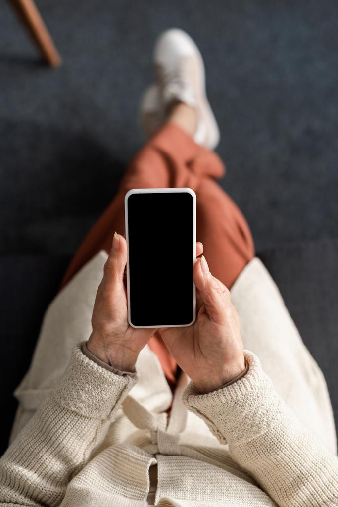 vista superior de la mujer mayor sosteniendo teléfono inteligente con pantalla en blanco
 - Foto, imagen