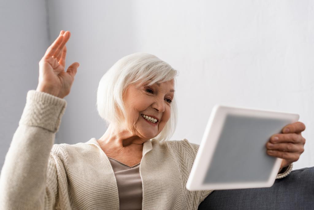 весела старша жінка сидить з піднятою рукою під час використання цифрового планшета
 - Фото, зображення