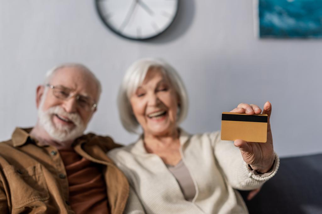 selektywne skupienie się na szczęśliwej seniorce pokazującej kartę kredytową w pobliżu uśmiechniętego męża - Zdjęcie, obraz