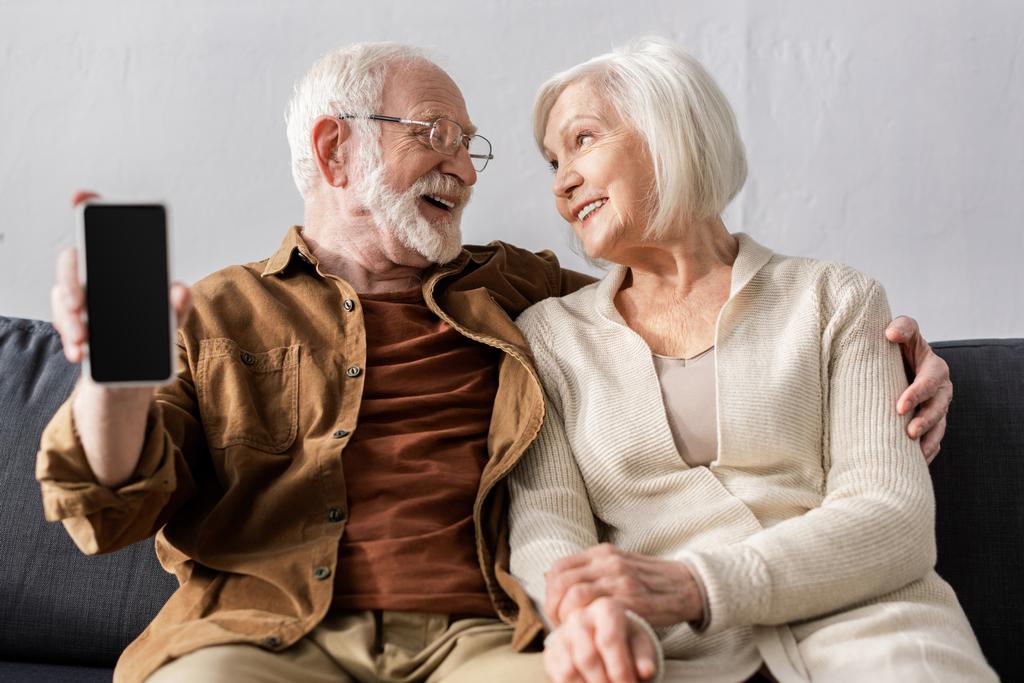 feliz hombre mayor mostrando teléfono inteligente con pantalla en blanco mientras mira a la esposa sonriente
 - Foto, imagen