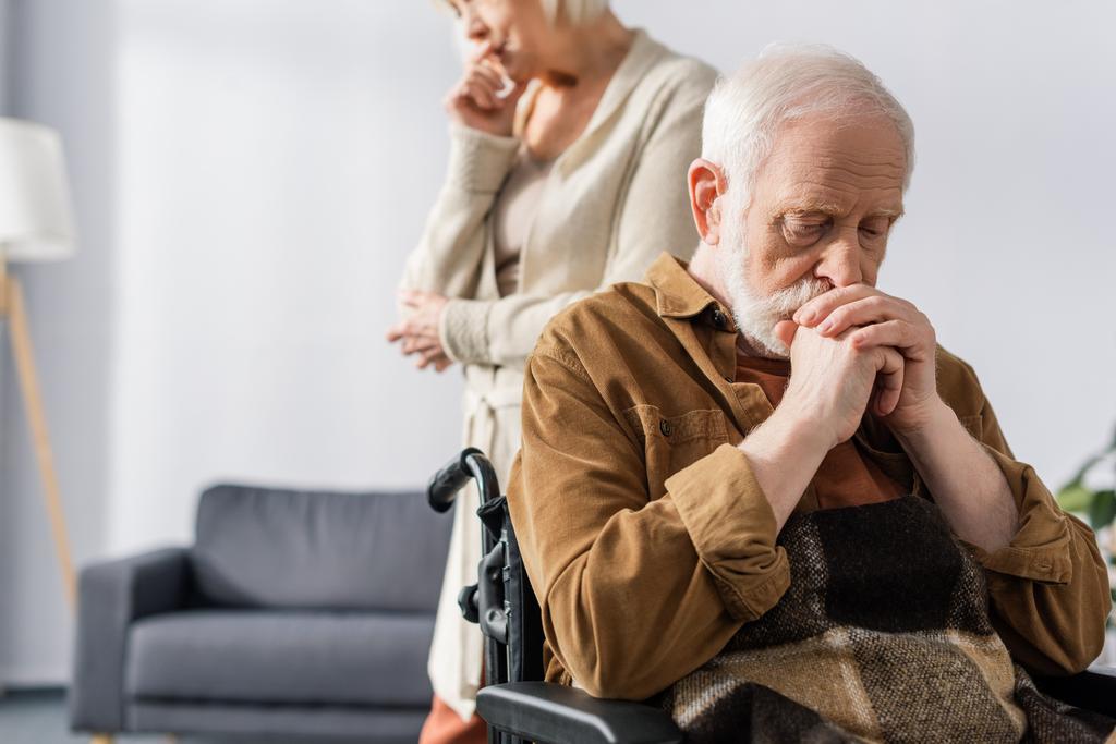 vista recortada de la triste mujer mayor de pie cerca de discapacitados, marido enfermo sentado en silla de ruedas con las manos apretadas
  - Foto, Imagen